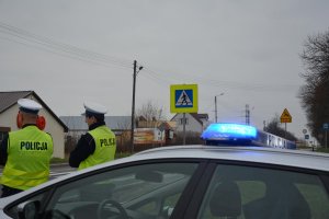 policjanci stojąc przed radiowozem obserwują ruch na drodze