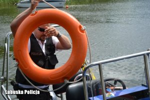 policjant będąc na łodzi, trzyma koło ratunkowe