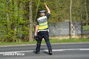 policjant podnosi rękę do góry dając znać kierowcy do zatrzymania się